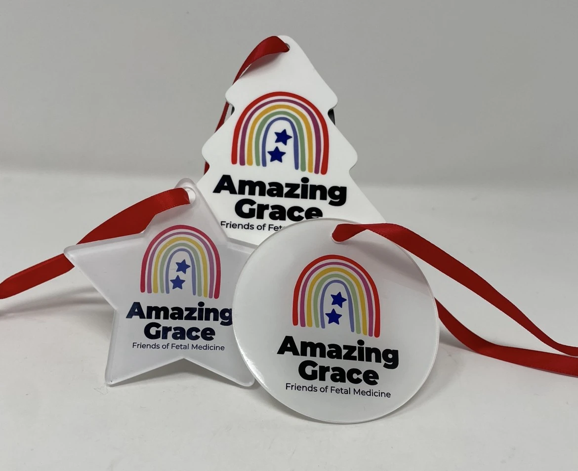 Flat plastic Amazing Grace Christmas decorations (tree, star, bauble) with logo and “Amazing Grace Friends of Fetal Medicine,” hanging with red ribbons